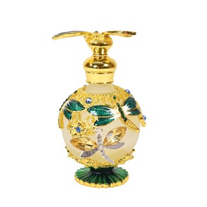 May include: A gold and green glass perfume bottle with a dragonfly design. The bottle has a round body and a small, decorative base.