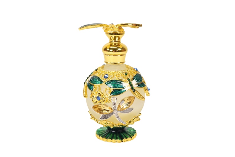 May include: A gold and green glass perfume bottle with a dragonfly design. The bottle has a round body and a small, decorative base.