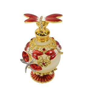 May include: A white glass perfume bottle with a gold and red dragonfly design. The bottle has a round body and a decorative base. The dragonfly is perched on the top of the bottle.