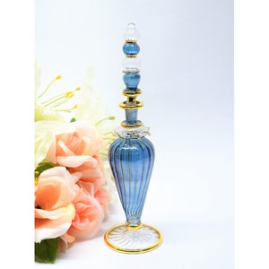 May include: A blue glass perfume bottle with gold accents and a clear glass stopper. The bottle has a ribbed design and a round base.