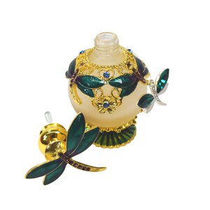 May include: A gold and green glass perfume bottle with a dragonfly design. The bottle has a clear glass stopper with a gold top and a dragonfly design.