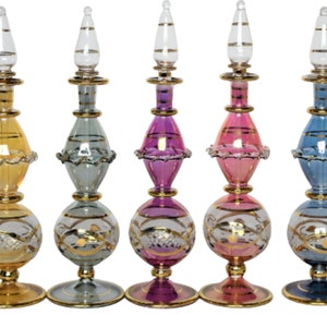 May include: Five decorative glass perfume bottles with gold accents. The bottles are in various colours, including yellow, blue, pink, and clear. Each bottle has a round base and a slender neck with a gold stopper.