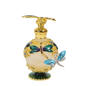 May include: A gold and green glass perfume bottle with a dragonfly design. The bottle has a gold cap and a dragonfly charm hanging from it.