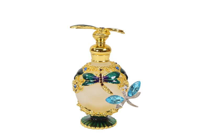 May include: A gold and green glass perfume bottle with a dragonfly design. The bottle has a gold cap and a dragonfly charm hanging from it.