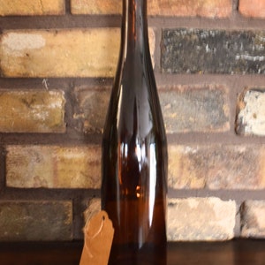 Puede incluir: Una botella de vidrio marr&oacute;n con un tap&oacute;n de corcho y una etiqueta de papel marr&oacute;n que dice "To Gift". La botella est&aacute; sobre una superficie de madera marr&oacute;n oscura.