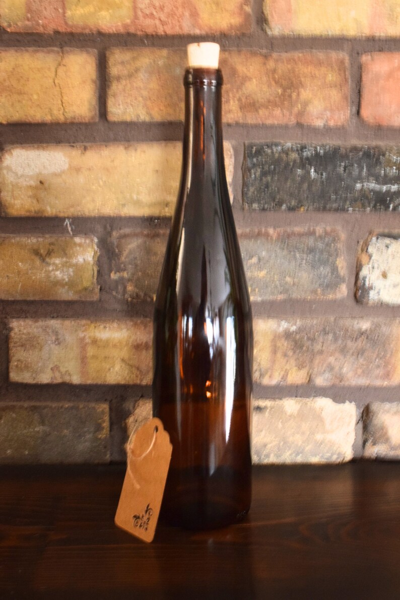 Puede incluir: Una botella de vidrio marr&oacute;n con un tap&oacute;n de corcho y una etiqueta de papel marr&oacute;n que dice "To Gift". La botella est&aacute; sobre una superficie de madera marr&oacute;n oscura.