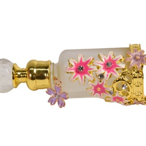 May include: A gold-colored perfume bottle with a clear glass body and a decorative floral design. The bottle has a white, crystal-like stopper and a gold-colored stand with floral accents.