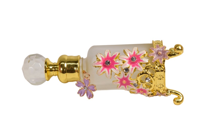 May include: A gold-colored perfume bottle with a clear glass body and a decorative floral design. The bottle has a white, crystal-like stopper and a gold-colored stand with floral accents.