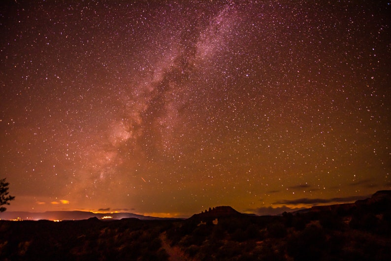 May include: A night sky with a vast expanse of stars, including the Milky Way, visible above a dark silhouette of a mountain range.