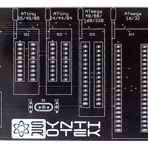 Może przedstawiać: Czarna płytka drukowana z czterema rzędami pinów oznaczonych jako "ATtiny 25/45/85", "ATtiny 24/44/84", "ATmega 48/88/168/328" i "ATmega 16/32". Płytka ma również logo z napisem "SYNTH ROTEK".