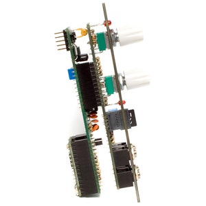 May include: A green circuit board with multiple black connectors, two white knobs, and a small gray chip. The board is mounted on a metal stand.