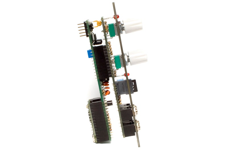 May include: A green circuit board with multiple black connectors, two white knobs, and a small gray chip. The board is mounted on a metal stand.
