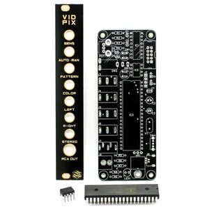 Op de afbeelding: Een zwart printplaat met gouden letters en componenten, een zwart paneel met gouden letters en ronde uitsparingen, en twee zwarte geïntegreerde schakelingen.