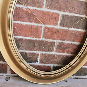 May include: An oval picture frame with a metallic gold finish and a smooth, rounded profile. The frame features a thin, light-colored string attached to the inner top edge for hanging purposes, showcasing a simple and clean design structure.