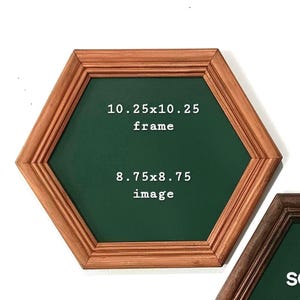 May include: A hexagonal wooden picture frame with a light brown finish and a dark green interior. The text on the green surface reads 10.25x10.25 frame and 8.75x8.75 image, indicating the outer dimensions in inches and the inner image area.