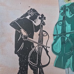 Op de afbeelding: Een zwart-wit linoleumsnede van een persoon die cello speelt, met een koptelefoon. De afdruk staat op een beige achtergrond. Rechts staat een turquoise linoleumsnede van een cello. De cello heeft een gebogen body en vier snaren.