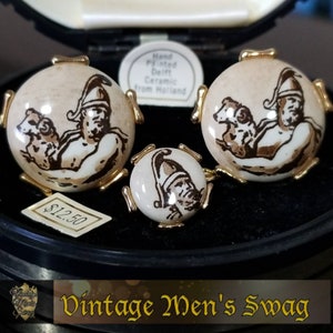 Könnte beinhalten: Ein Set aus drei Vintage-Manschettenknöpfen mit handbemalten Designs aus Delft-Keramik. Die Manschettenknöpfe zeigen einen Mann, der einen Widder hält, in einem braunen und weißen Farbschema. Die Manschettenknöpfe werden in einer schwarzen Samtbox mit einem Preisschild von 12,50 € präsentiert.