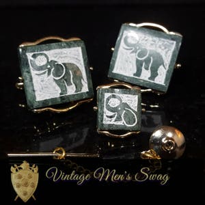 May include: A set of three green and gold cufflinks and a tie tack featuring white elephant designs.  The cufflinks and tie tack are made of a green stone with a gold metal frame.  The elephants are carved into the stone and are white in color.
