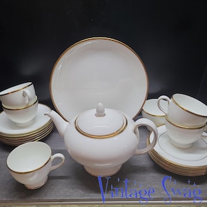 May include: A white tea set with gold trim. The set includes a teapot, a serving plate, and four teacups and saucers.