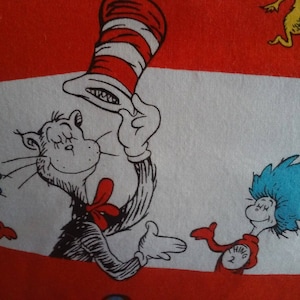 May include: A red, white, and black fabric with a cartoon illustration of the Cat in the Hat, Thing 1, and Thing 2. The Cat in the Hat is wearing a red and white striped hat. Thing 1 is wearing a red and white striped shirt with the words "Thing 1" on it. Thing 2 is wearing a red and white striped shirt with the words "Thing 2" on it.