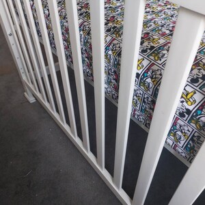 May include: White crib with white wooden slats and a fitted sheet with a cartoon character print. The sheet features a repeating pattern of Mickey Mouse, Donald Duck, Goofy, and Pluto.