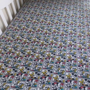 May include: A white crib sheet with a repeating pattern of Mickey Mouse, Donald Duck, and Goofy in colorful comic book frames.