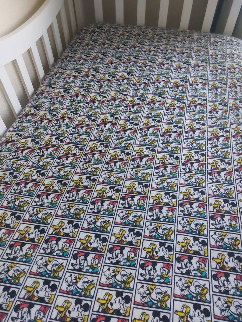 May include: A white crib sheet with a repeating pattern of Mickey Mouse, Donald Duck, and Goofy in colorful comic book frames.