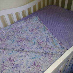 May include: A white crib with a purple and white patterned blanket. The blanket has a design of multiple cartoon mermaids.