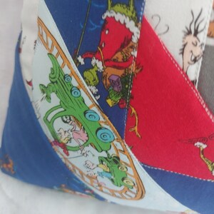 Peut inclure: Un oreiller patchwork color&eacute; avec un fond bleu, rouge et blanc. L'oreiller pr&eacute;sente une voiture verte avec des personnes &agrave; l'int&eacute;rieur, une figure rouge avec un chapeau vert et une figure blanche avec un chapeau noir. L'oreiller est fait de diff&eacute;rents tissus et a un design cousu.