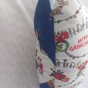 Peut inclure: Un oreiller blanc et bleu sur le th&egrave;me de No&euml;l. L'oreiller pr&eacute;sente un motif r&eacute;p&eacute;titif de personnages du livre "Comment le Grinch a vol&eacute; No&euml;l !" et le texte "Joyeux Grinchmas".