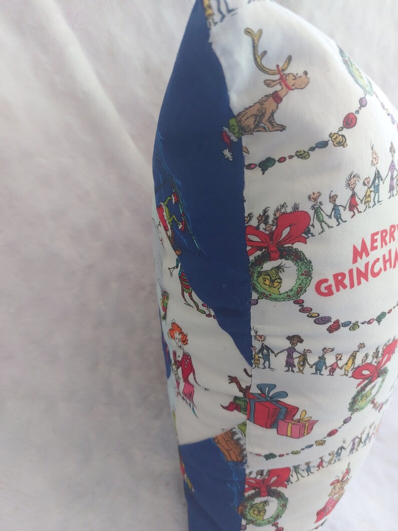 Peut inclure: Un oreiller blanc et bleu sur le th&egrave;me de No&euml;l. L'oreiller pr&eacute;sente un motif r&eacute;p&eacute;titif de personnages du livre "Comment le Grinch a vol&eacute; No&euml;l !" et le texte "Joyeux Grinchmas".