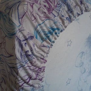 May include: A white fabric with a blue and purple floral pattern. The fabric has a ruffled edge and is decorated with stars.