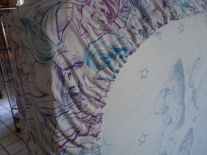 May include: A white fabric with a blue and purple floral pattern. The fabric has a ruffled edge and is decorated with stars.