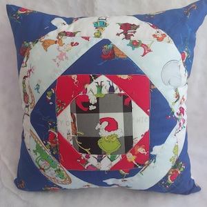 Peut inclure: Un oreiller bleu et blanc avec un motif &agrave; carreaux rouge et blanc au centre. L'oreiller est d&eacute;cor&eacute; de carr&eacute;s de tissu color&eacute;s repr&eacute;sentant des personnages du dessin anim&eacute; du Grinch. Le carr&eacute; central repr&eacute;sente le Grinch portant un chapeau de P&egrave;re No&euml;l.