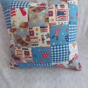 May include: A patchwork pillow with a red, white, and blue theme. The pillow is made of different fabrics with various patriotic designs, including stars, stripes, and roosters. The text "USA", "AMERICA", "FREEDOM", "LIBERTY", and "JULY 4TH" is visible on the pillow.