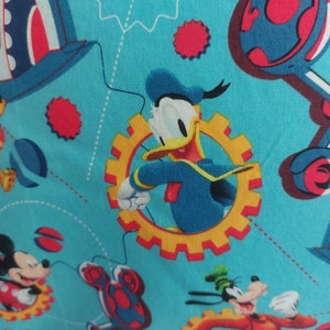 May include: A blue fabric with a repeating pattern of cartoon characters, including Mickey Mouse, Donald Duck, and Goofy. The characters are depicted in a whimsical style, with bright colors and bold outlines. The fabric features a blue background with yellow, red, and white accents.
