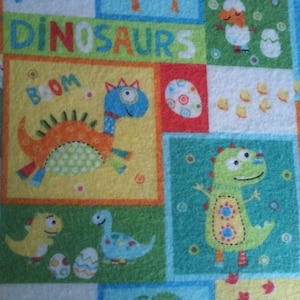 May include: Colorful dinosaur-themed fabric with a repeating pattern of cartoon dinosaurs, eggs, and the word "DINOSAURS". The dinosaurs are in various colors, including blue, orange, and green, set against a patchwork background.
