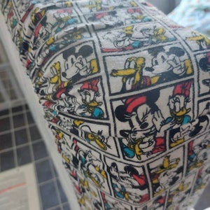 May include: White fabric with a repeating pattern of Mickey Mouse and Donald Duck cartoon characters in comic book panels. The characters are in black, red, yellow, and blue.
