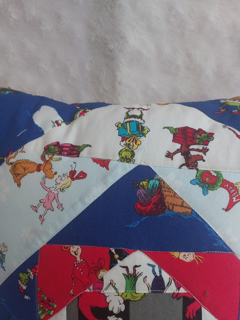 Peut inclure: Un coussin en patchwork color&eacute; repr&eacute;sentant des personnages du livre "Comment le Grinch a vol&eacute; No&euml;l !" Le coussin est fait de diff&eacute;rents tissus, dont du rouge, du bleu, du blanc et du vert. Le coussin est d&eacute;cor&eacute; de divers personnages, dont le Grinch, Cindy Lou Who et Max le chien.