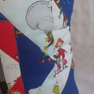 Peut inclure: Un coussin patchwork bleu, rouge, blanc et vert sur le th&egrave;me de No&euml;l. Le coussin pr&eacute;sente des personnages du livre "Comment le Grinch a vol&eacute; No&euml;l !" dont le Grinch, Cindy Lou Who et Max le chien.