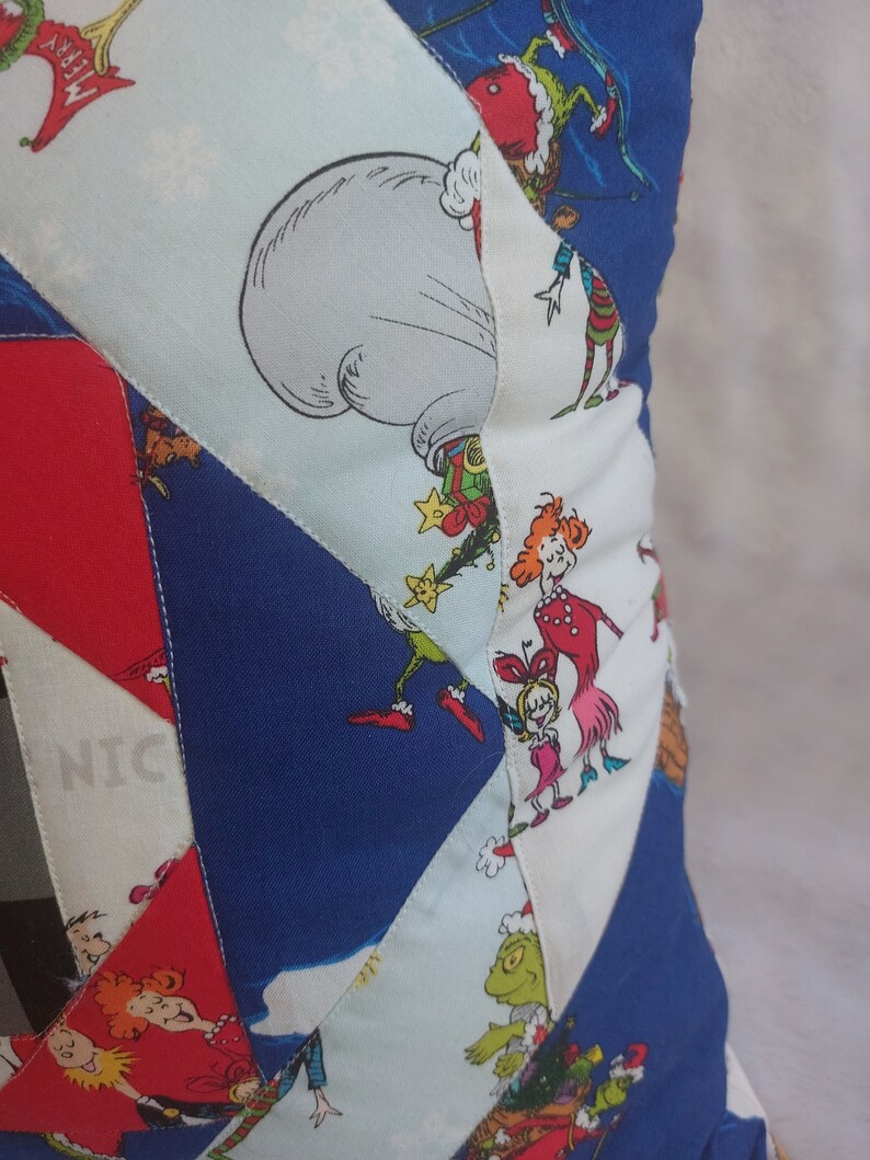 Peut inclure: Un coussin patchwork bleu, rouge, blanc et vert sur le th&egrave;me de No&euml;l. Le coussin pr&eacute;sente des personnages du livre "Comment le Grinch a vol&eacute; No&euml;l !" dont le Grinch, Cindy Lou Who et Max le chien.