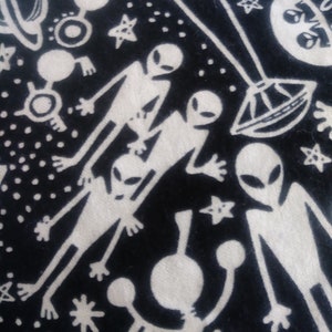 May include: Black fabric with a white design of aliens, stars, and planets. The aliens are depicted with large heads and small bodies.