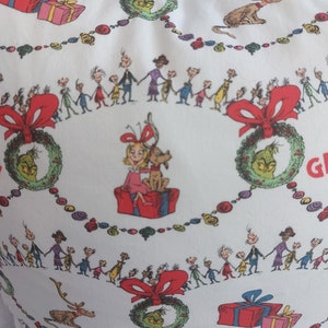 Peut inclure: Housse de coussin blanche avec un motif de No&euml;l festif repr&eacute;sentant le Grinch, un renne et un groupe d'enfants. Le motif comprend des couronnes, des cadeaux et les mots "Joyeux No&euml;l".
