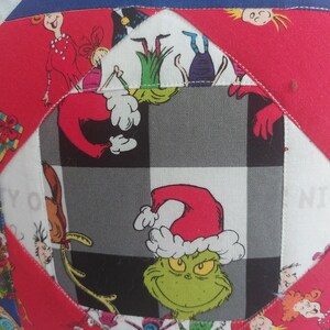 Peut inclure: Un tissu &agrave; carreaux rouge, blanc et noir avec un personnage vert du Grinch portant un chapeau de P&egrave;re No&euml;l rouge. Le Grinch est entour&eacute; d'autres carr&eacute;s de tissu color&eacute;s avec des personnages de dessins anim&eacute;s.