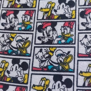 May include: A white fabric with a repeating pattern of cartoon characters. The characters are Mickey Mouse, Donald Duck, and Goofy. The characters are in different poses and expressions. The fabric is a light white with black outlines around each character.