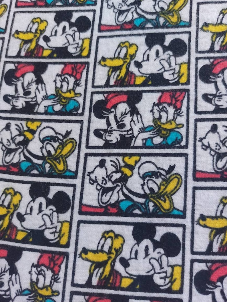 May include: A white fabric with a repeating pattern of cartoon characters. The characters are Mickey Mouse, Donald Duck, and Goofy. The characters are in different poses and expressions. The fabric is a light white with black outlines around each character.