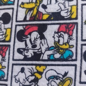 May include: A white fabric with a repeating pattern of cartoon characters. The characters include Mickey Mouse, Minnie Mouse, Donald Duck, and Goofy. The characters are in black, yellow, red, and blue.