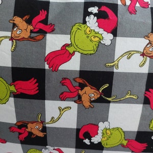 May include: Fabric with a black, white, and gray checkered pattern featuring cartoon characters. The characters include a green creature wearing a Santa hat and a brown reindeer-like character with red scarves.