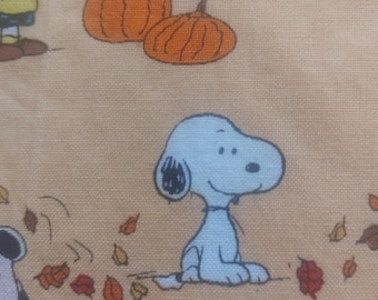Peut inclure: Un tissu beige clair avec un motif répétitif représentant les personnages des Peanuts, dont Snoopy, Charlie Brown et Lucy. Le design comprend des citrouilles orange et des feuilles d'automne éparpillées dans des tons rouge, brun et jaune.