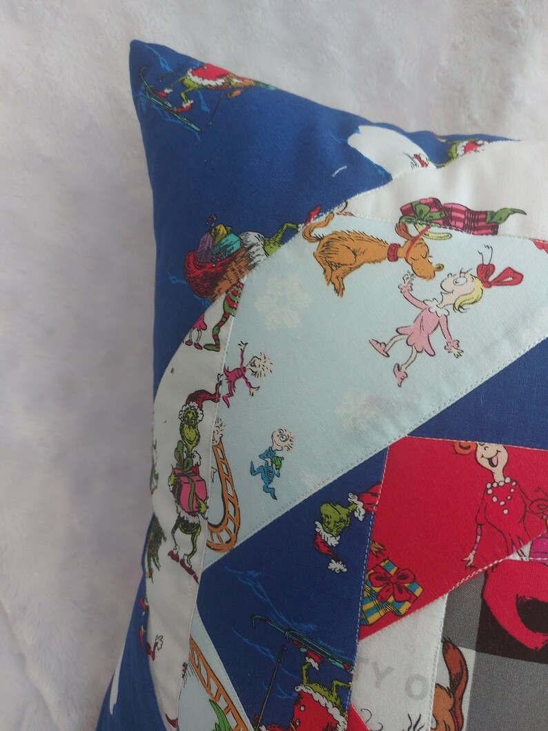 Peut inclure: Une housse de coussin en patchwork bleu et blanc sur le th&egrave;me de No&euml;l. Le tissu pr&eacute;sente une vari&eacute;t&eacute; de personnages du livre "Comment le Grinch a vol&eacute; No&euml;l !" dont le Grinch, Cindy Lou Who et Max le chien.